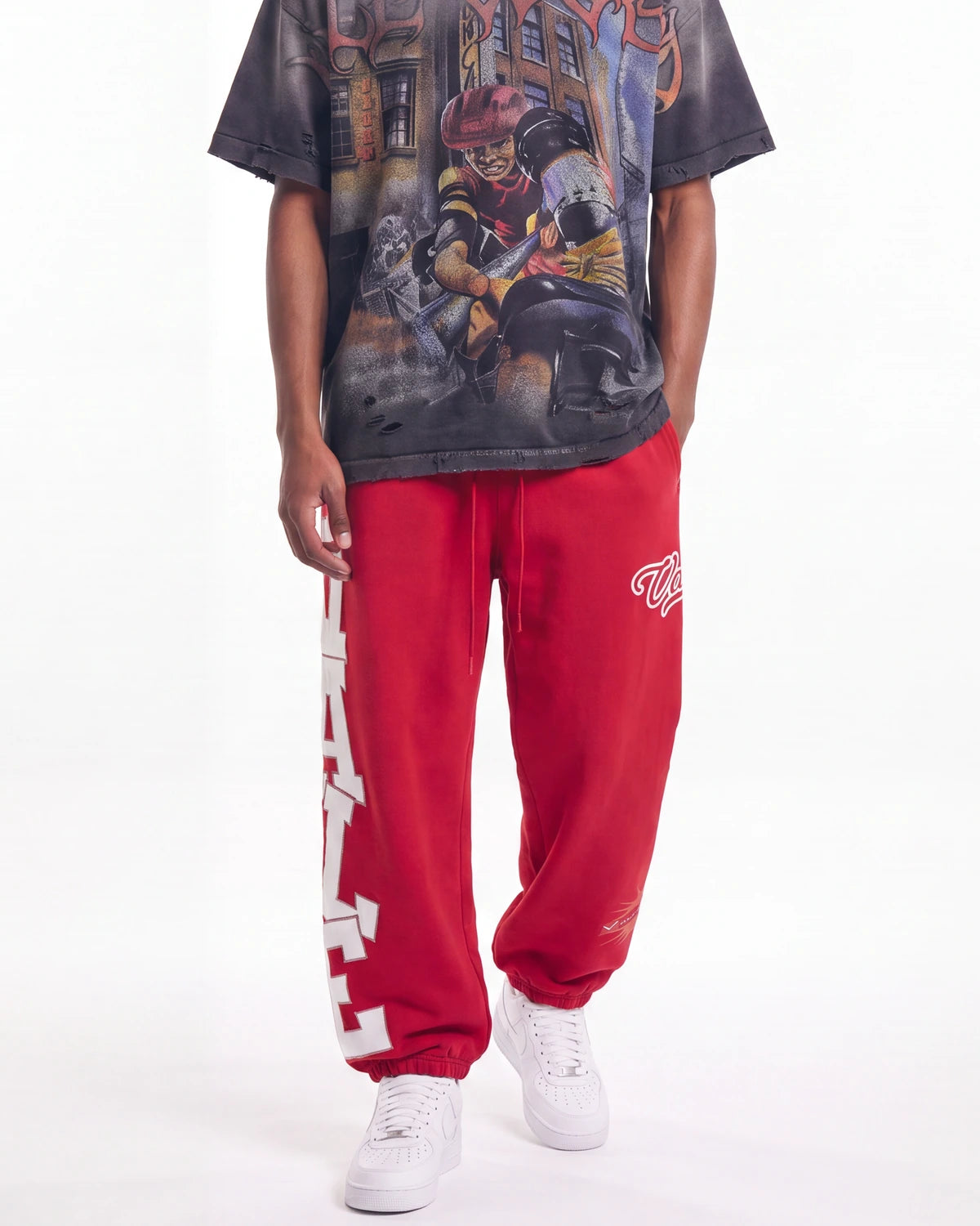 A model wearing red sweatpants with white graphic lettering down the side and white sneakers, paired with a graphic t-shirt, against a plain white studio background.