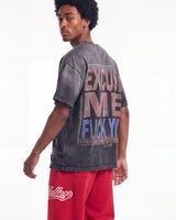 A man wearing a faded charcoal gray graphic t-shirt with a large back print reading 'EXCUSE ME FUCK YO' in pink, purple, and blue, paired with red sweatpants, photographed against a white studio background.