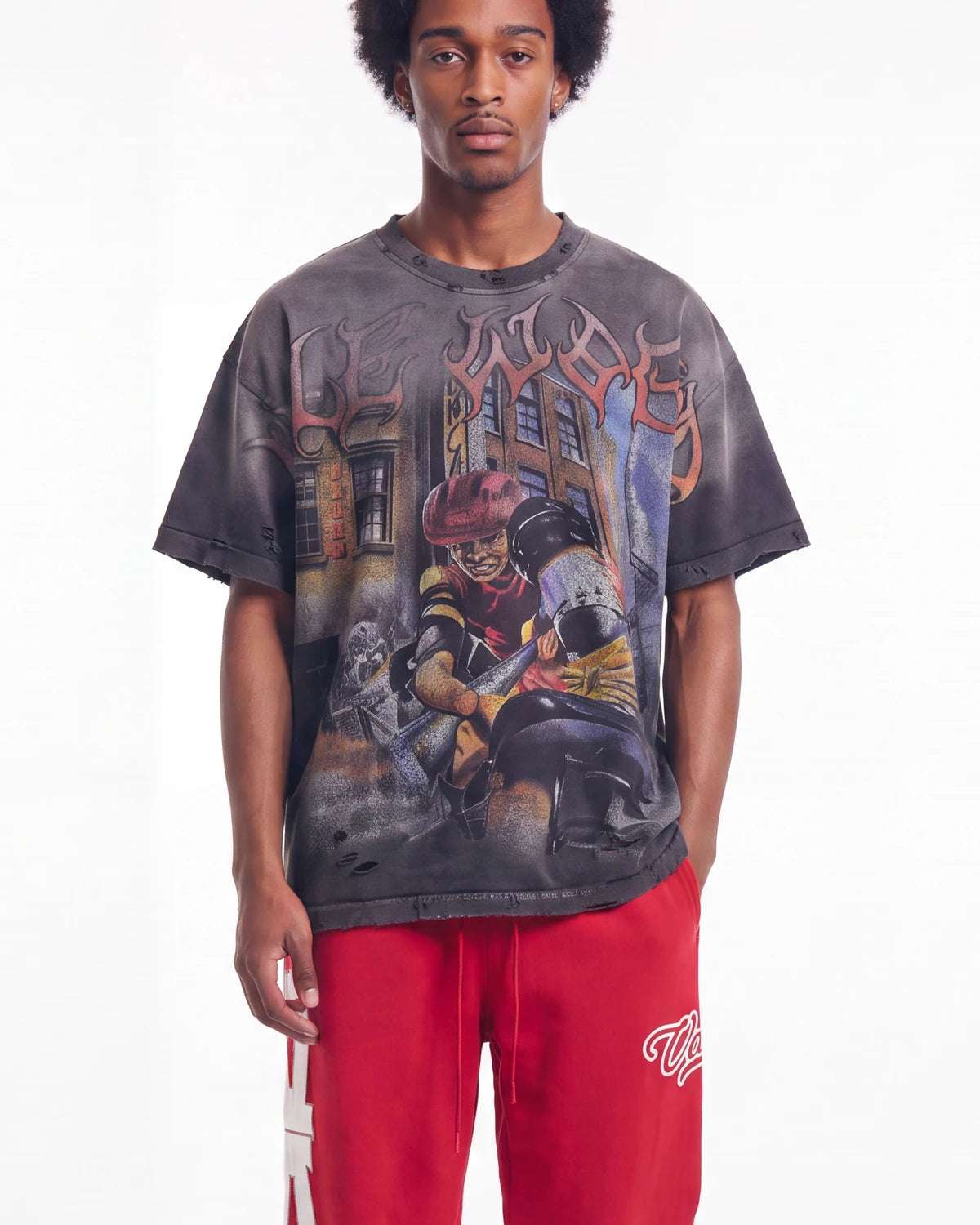 A model wearing a faded black graphic t-shirt with a detailed street art print and red sweatpants, photographed against a solid white background.