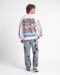 A model shown from the back wearing a white crewneck sweatshirt with a large colorful graffiti-style graphic print on the back and sleeves, paired with light-wash jeans and sneakers, against a plain white studio background.