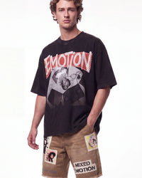 A male model wearing a black graphic t-shirt with a distressed red and white 'EMOTION' logo and a grayscale photo print, paired with tan shorts featuring patchwork details and 'MIXED EMOTION' text.