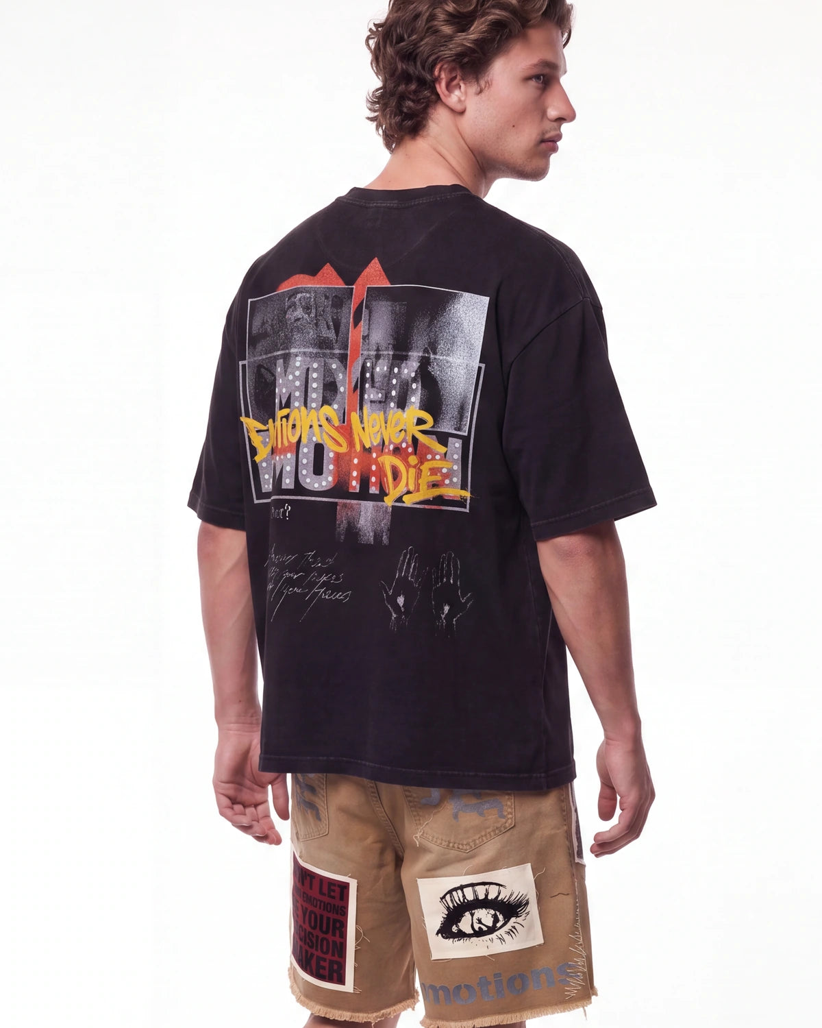 A man shown from the back wearing a faded black graphic t-shirt with a large 'This Is What We Do' design, paired with tan shorts, against a plain white background.