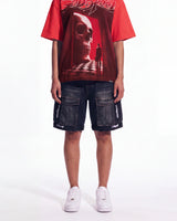 A model wearing a red t-shirt with a large red and black skull graphic, paired with dark denim cargo shorts and white sneakers, shown from the chest down on a white studio background.