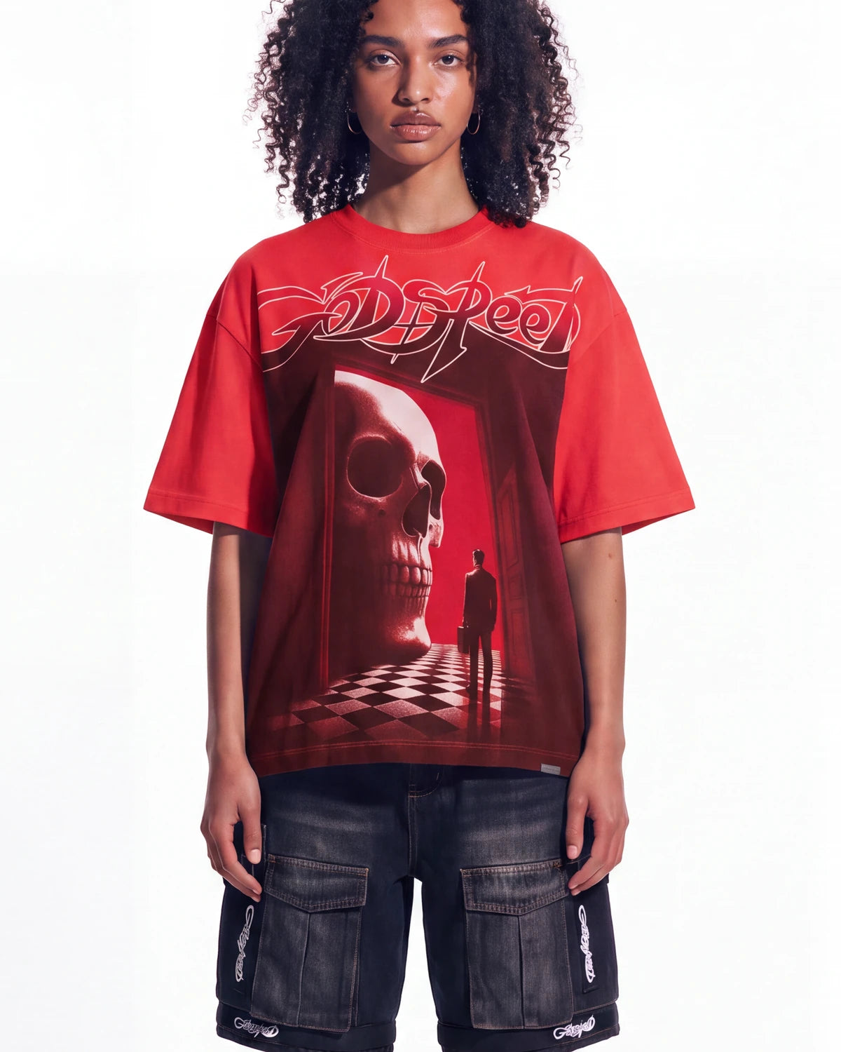 A model wearing a red Godspeed t-shirt with a large skull graphic and dark cargo shorts, photographed against a solid white background.