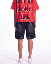 A model from the back wearing a bright red graphic t-shirt with bold black and white lettering, black cargo shorts with white logo details, and white sneakers, set against a plain white studio background.