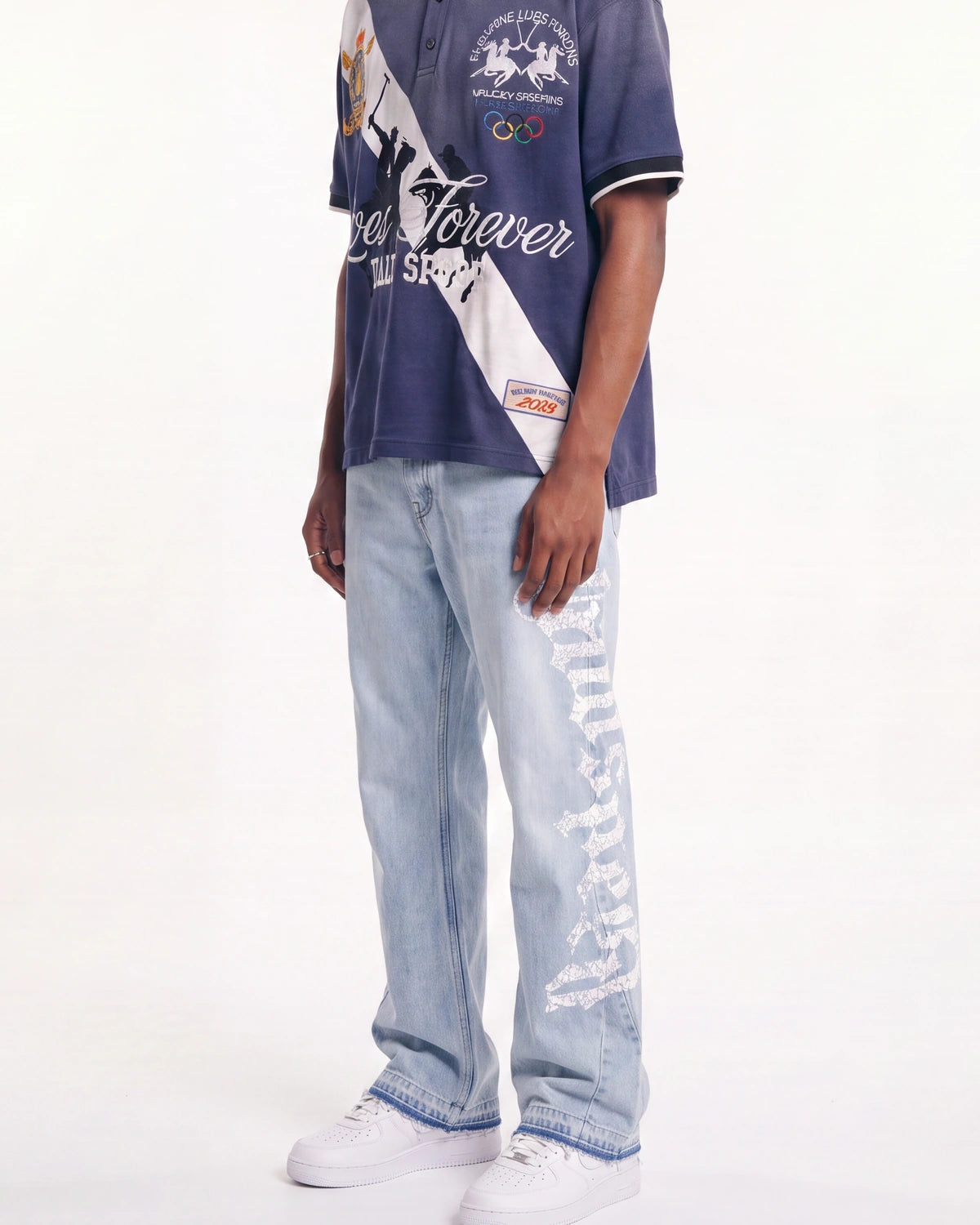 A model wearing a navy blue and white graphic polo shirt, light-wash distressed jeans with ripped details, and white sneakers, shown from the chest down against a plain white background.