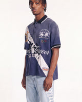 A man wearing a navy blue and white graphic polo shirt with 'Forever Your Style' text and horse racing graphics, paired with light-wash ripped jeans, against a plain white studio background.