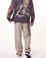 A person shown from the back wearing a dark gray long-sleeve graphic shirt with anime artwork and the text 'NILEYSEAN BEASTS' across the back, paired with light beige sweatpants and black-and-white sneakers, against a plain white studio background.