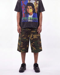 A model wearing a faded black graphic t-shirt with a colorful 'Famous Celebrity' Michael Jackson print, paired with green and brown camouflage shorts and black sneakers, against a plain white background.