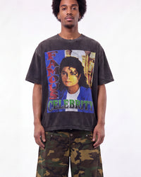 A man wearing a faded black graphic t-shirt featuring a colorful print of Michael Jackson with the text 'FAMOUS CELEBRITY', paired with green camouflage pants, against a plain white background.