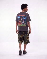 A man shown from the back wearing a dark gray graphic t-shirt with a large 'Psycho' print, paired with green and brown camouflage shorts, against a plain white studio background.