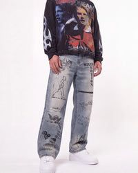 A person wearing a black long-sleeve graphic sweatshirt with football player prints, light-wash distressed jeans covered in graffiti-style drawings and text, and white sneakers, photographed against a plain white studio background.