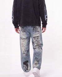 A person shown from the back wearing light-wash blue jeans with black graphic prints and a black sweatshirt against a plain white studio background.