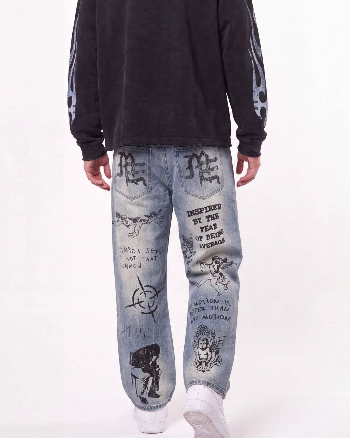 A person shown from the back wearing light-wash blue jeans with black graphic prints and a black sweatshirt against a plain white studio background.