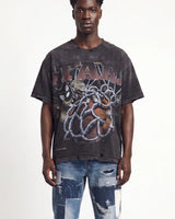A man wearing an oversized faded black graphic t-shirt with distressed details and a large front print, paired with ripped blue jeans, against a plain white background.