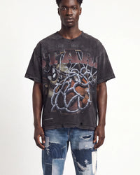 A man wearing an oversized faded black graphic t-shirt with distressed details and a large front print, paired with ripped blue jeans, against a plain white background.