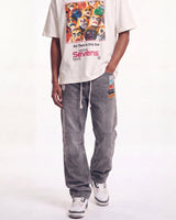 A person wearing a cream graphic T-shirt and faded gray baggy sweatpants with white sneakers, standing against a white studio background.
