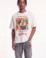 A man wearing an oversized off-white t-shirt with a colorful graphic print of faces and the text 'Deception Has Many Faces But There Is Only One Galaxy Sevens labels', paired with gray drawstring pants, against a plain white background.