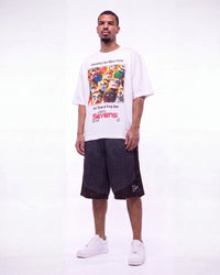 A man modeling a white graphic t-shirt with a colorful collage print and the text 'Sevens', paired with dark gray patterned shorts and white sneakers, against a plain white studio background.
