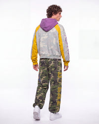 A model shown from the back wearing a gray and yellow color-block hoodie with a purple hood, paired with green camouflage sweatpants and white sneakers, against a plain white studio background.