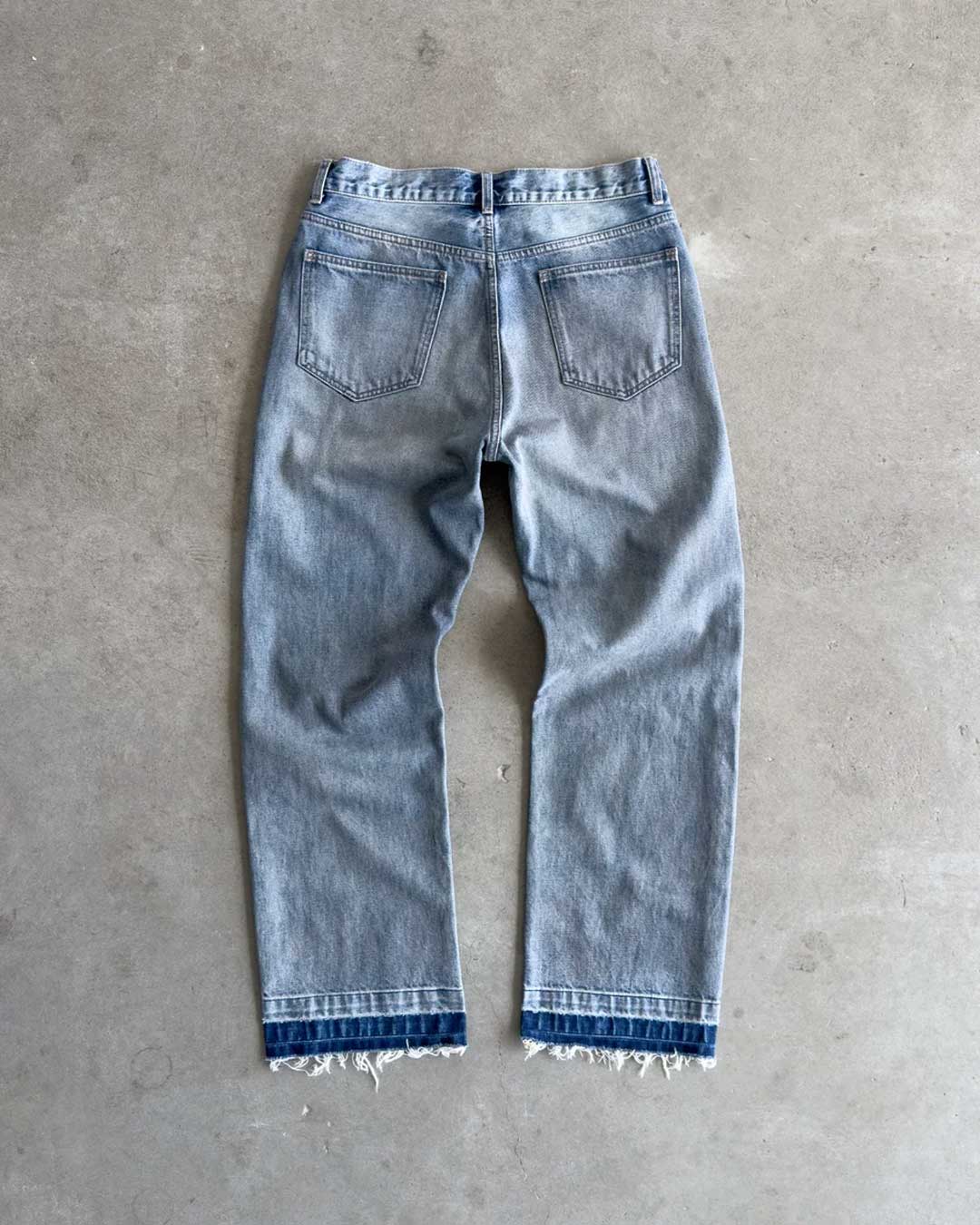 Bravest Studios Dirty Star Denim blue, flat-lay back view on concrete showing the frayed two-tone hem