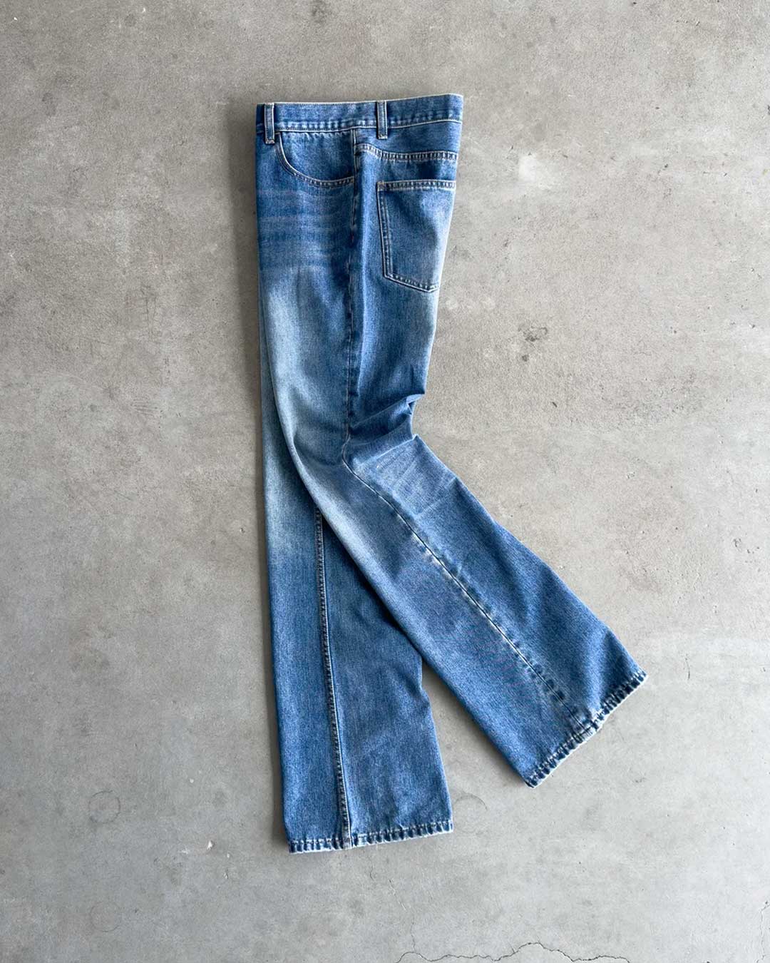 Bravest Studios Flare Denim Pants blue, flat-lay side view on concrete showing the boot-cut flare