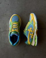 Bravest Studios Kross Kountry Runner Brazil, pair on concrete showing the blue mesh upper, green overlays and yellow cross applique