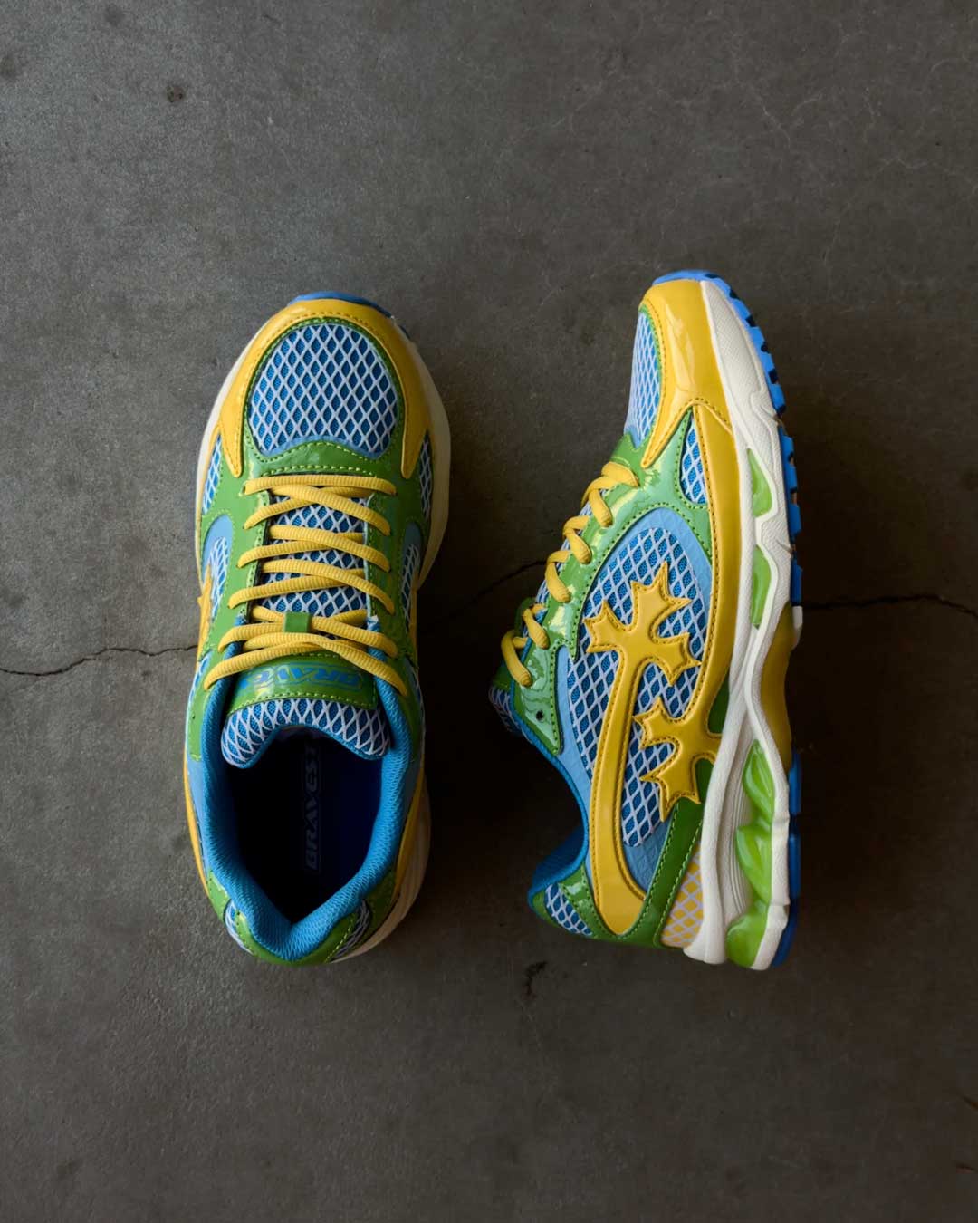 Bravest Studios Kross Kountry Runner Brazil, pair on concrete showing the blue mesh upper, green overlays and yellow cross applique