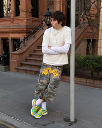 Bravest Studios Kross Kountry Runner Brazil, worn on a city sidewalk with camo cargo shorts and a cream tee, full outfit view