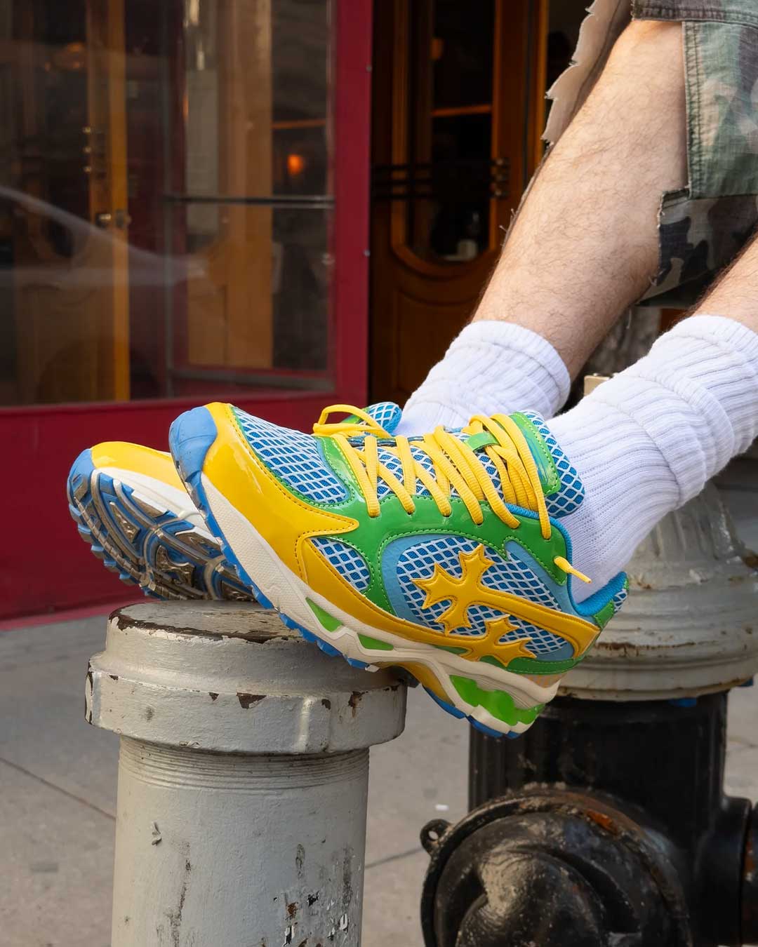 Bravest Studios Kross Kountry Runner Brazil, worn on foot propped on a sidewalk bollard showing the yellow laces and green midsole