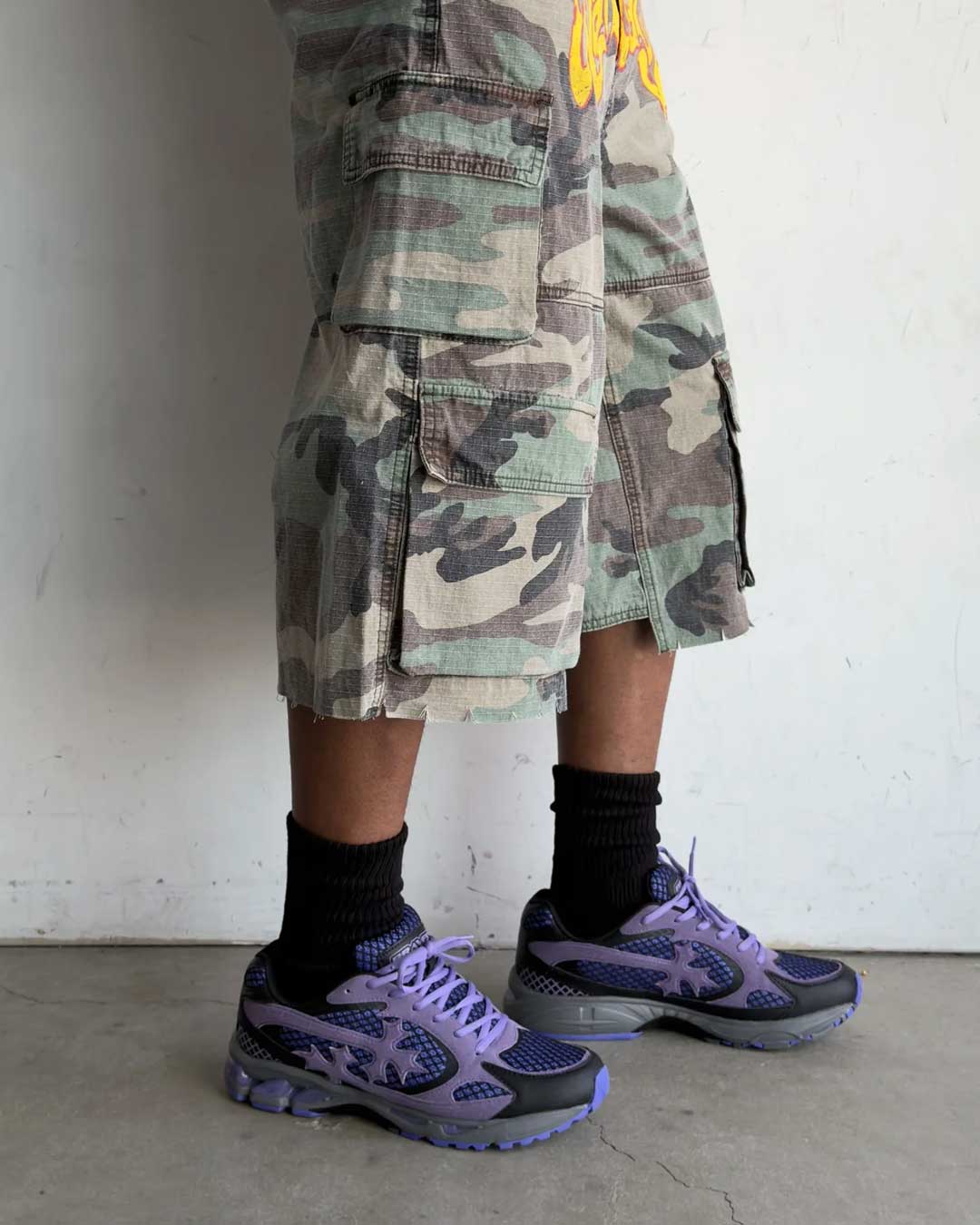 Bravest Studios Kross Kountry Runner Dirty Soda Purple, worn on foot with camo cargo shorts and black socks, full outfit view