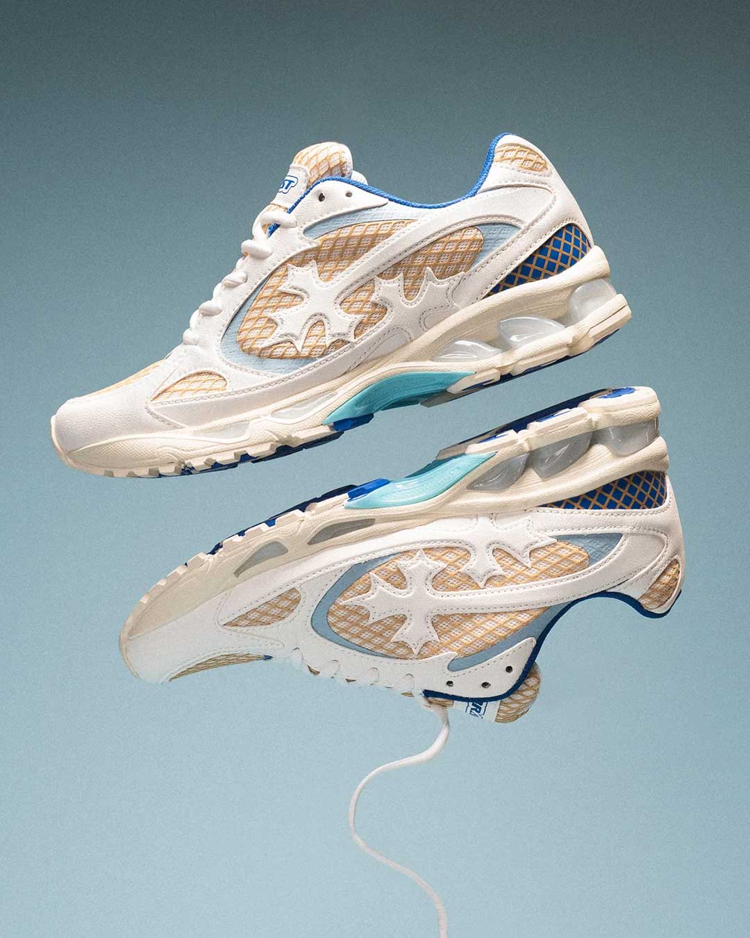 Bravest Studios Kross Kountry Runner Ice Blue, pair floating on a blue gradient backdrop showing the cream upper and ice-blue midsole pods