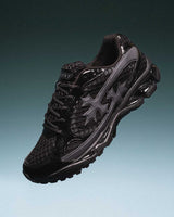 Bravest Studios Kross Kountry Runner Triple Black, single shoe angled on a teal gradient backdrop showing the gunmetal cross applique and lugged outsole