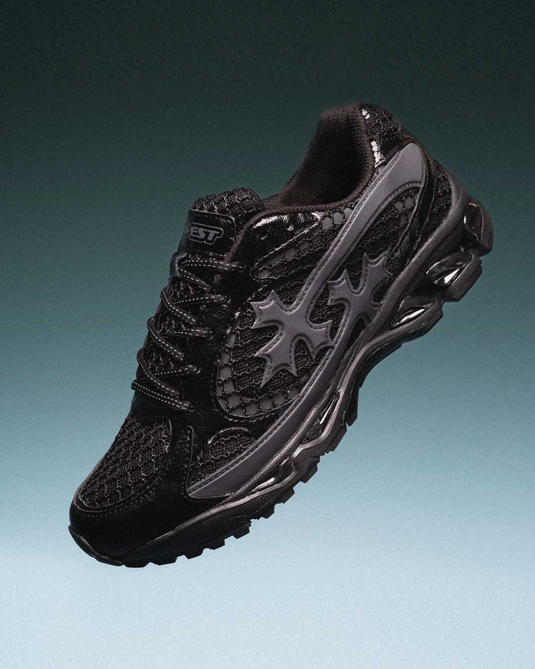 Bravest Studios Kross Kountry Runner Triple Black, single shoe angled on a teal gradient backdrop showing the gunmetal cross applique and lugged outsole