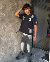 Bravest Studios Patch Polo black, worn by a model with baggy grey jeans, showing the boxy cropped fit