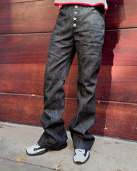 Bravest Studios Raw Flare Denim black, close model shot of the exposed button fly and the flared leg stacking over the shoe