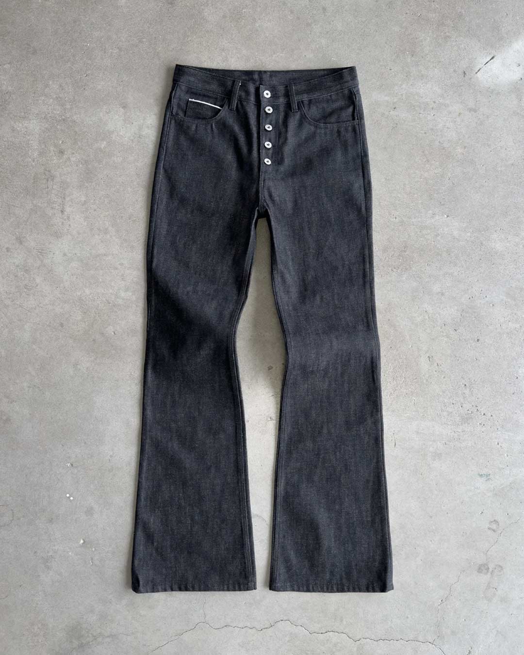 Bravest Studios Raw Flare Denim black, flat-lay front view on concrete showing the full flared silhouette