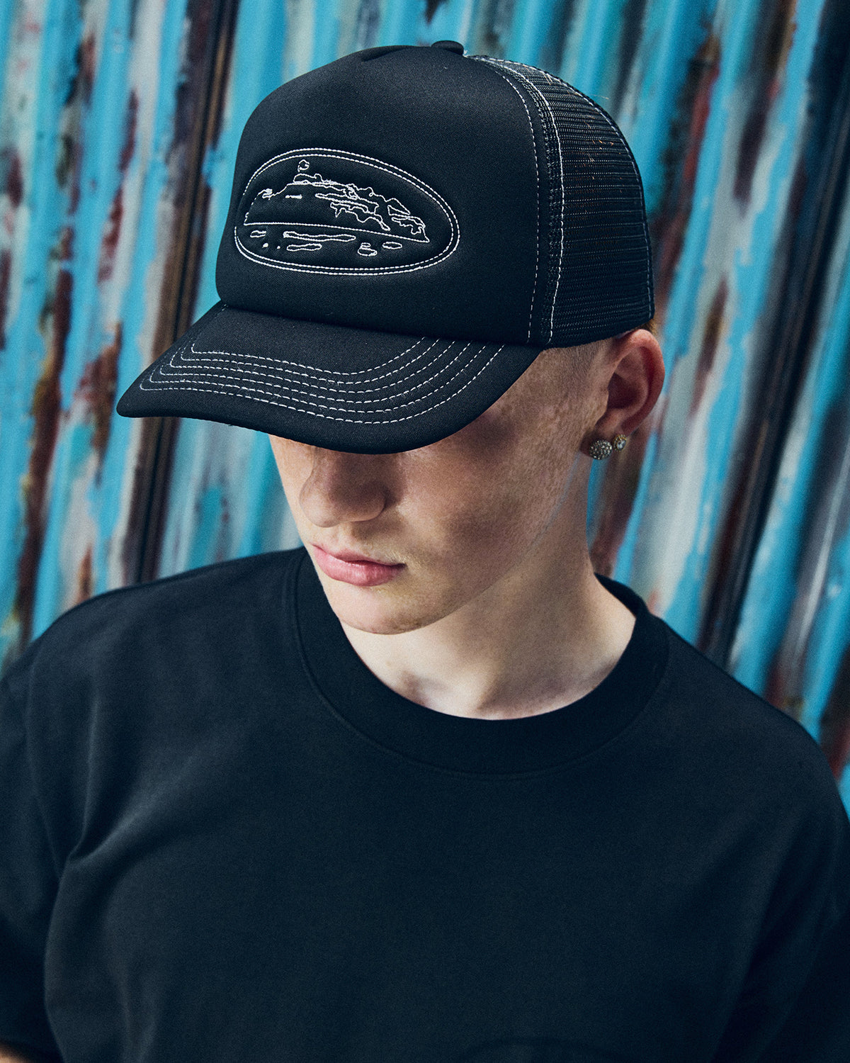 Corteiz Island Outline Trucker Hat black, worn by a model with a black tee, close front view