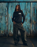 Corteiz OG Island LS Tee black, worn by a model with cargo pants, front view showing the small white chest island graphic