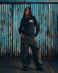 Corteiz OG Island LS Tee black, worn by a model with cargo pants, front view showing the small white chest island graphic