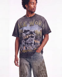 A man wearing a faded black graphic t-shirt with a wolf design and distressed gray jeans, standing against a white studio background.