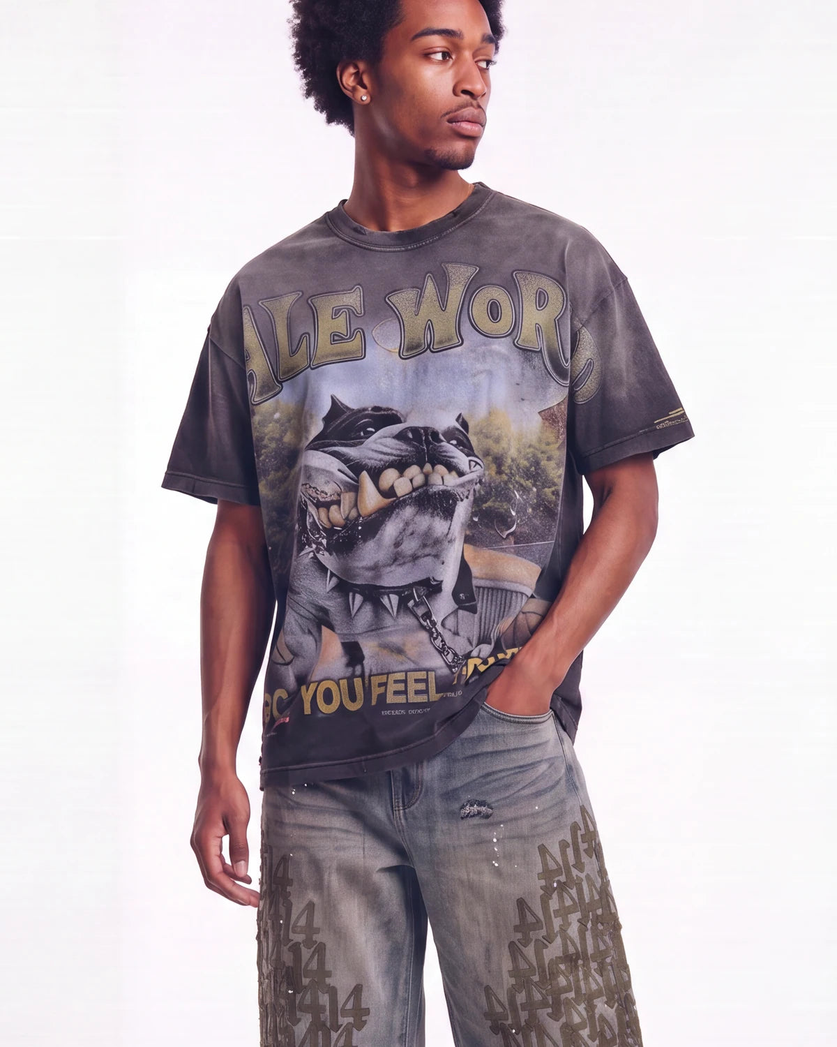 A man wearing a faded black graphic t-shirt with a wolf design and distressed gray jeans, standing against a white studio background.