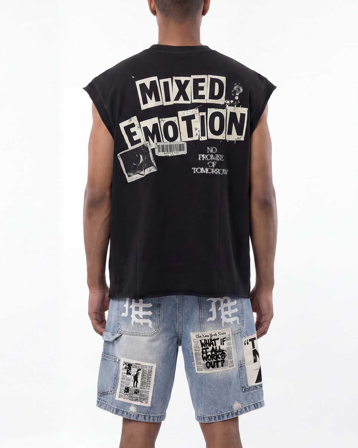 A man shown from the back wearing a black sleeveless t-shirt with a large white graphic print reading 'MIXED EMOTION' and light-wash denim shorts with patchwork details.