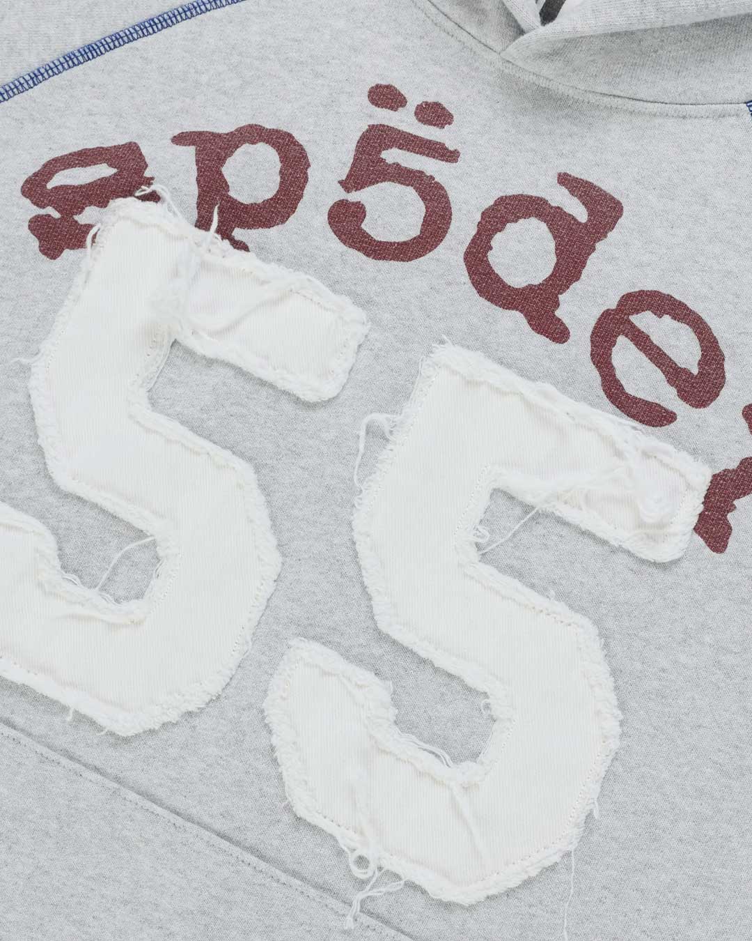 Sp5der 55 University Hoodie heather grey, close-up of the burgundy Sp5der lettering and distressed white 55 appliqué