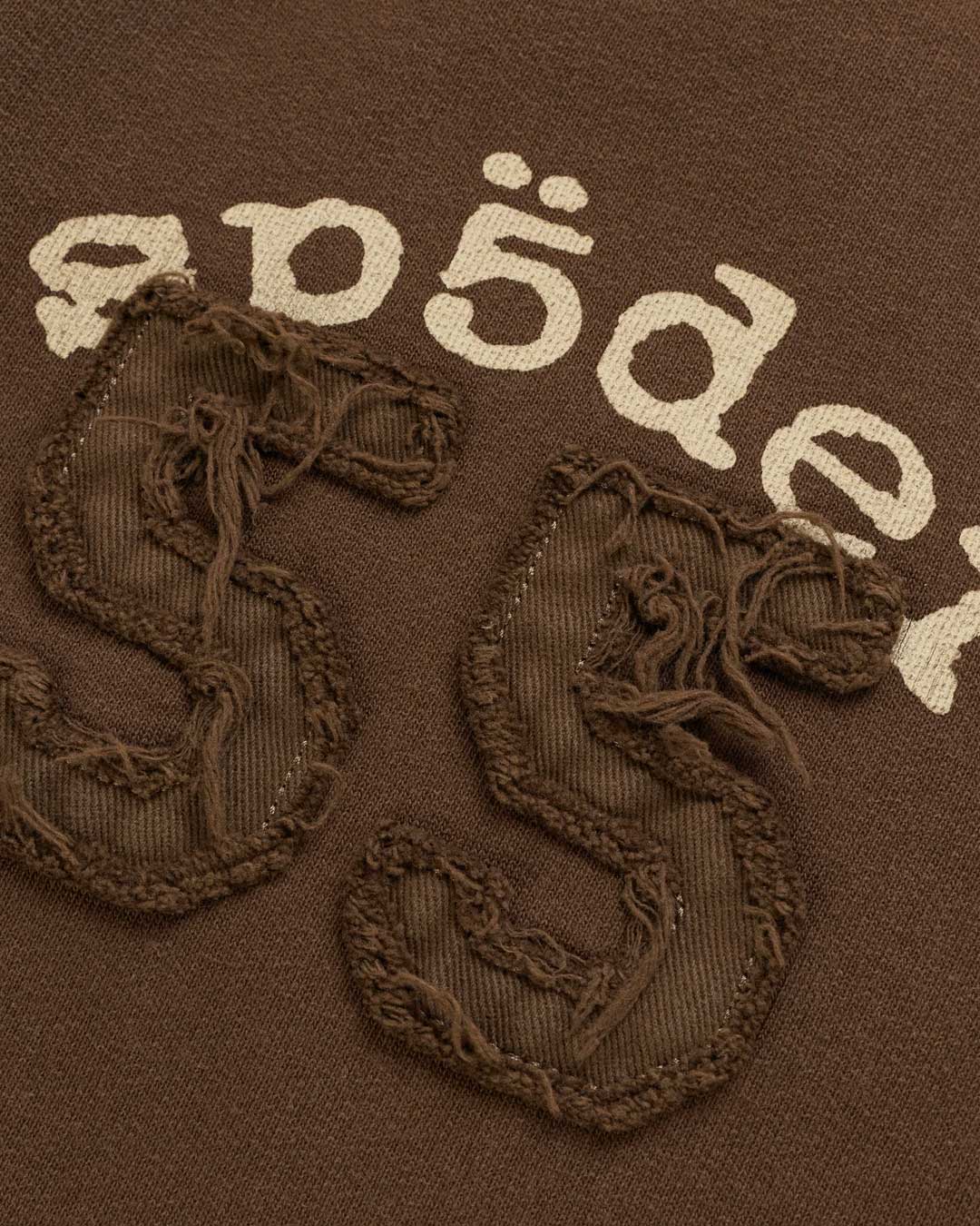 Sp5der 55 University Wide Leg Sweatpants brown, close-up of the Sp5der lettering and distressed 55 appliqué