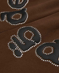 Sp5der OG Web Rhinestone Sweatpants brown, close-up of the black lettering outlined in silver rhinestones