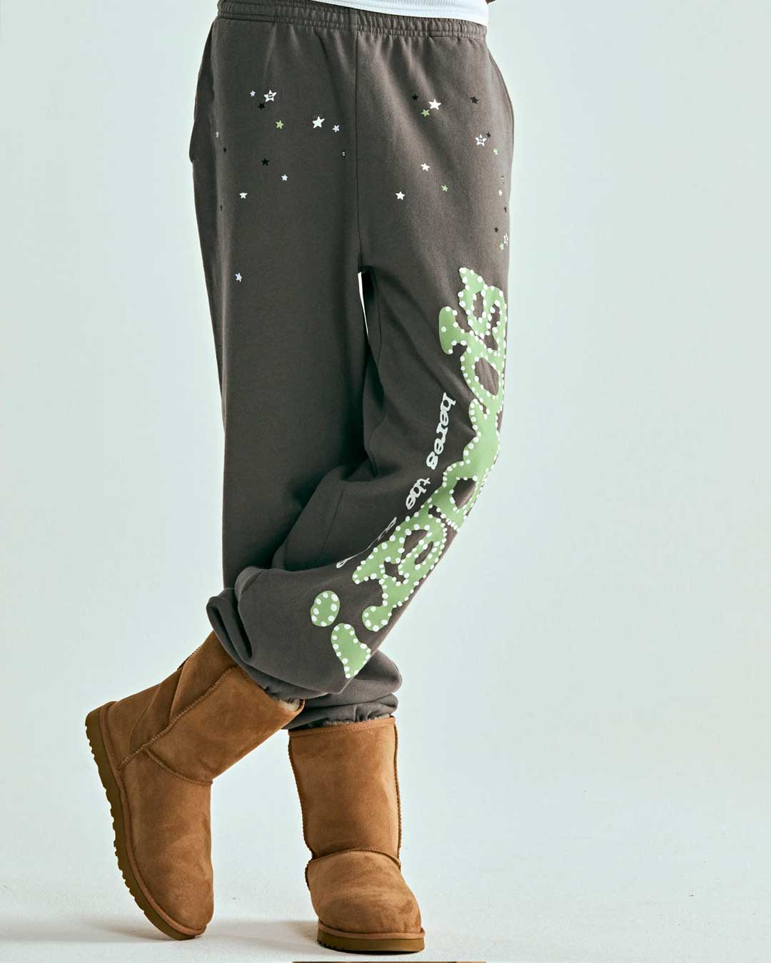 Sp5der P*nk V1 Sweatpants slate grey, worn on model, side view showing the green logo running down the leg