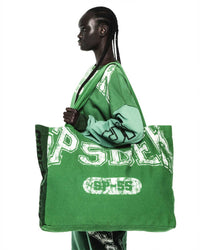 Sp5der Sp5 Jersey Tote Bag kelly green held at the shoulder by a model, front lettering and oval badge visible