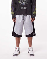 A model is shown from the waist down wearing a pair of Triple Seven black and white patterned athletic shorts with a drawstring, styled with a black graphic long-sleeve shirt and white sneakers.