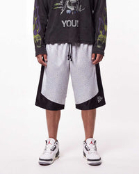 A model is shown from the waist down wearing a pair of Triple Seven black and white patterned athletic shorts with a drawstring, styled with a black graphic long-sleeve shirt and white sneakers.